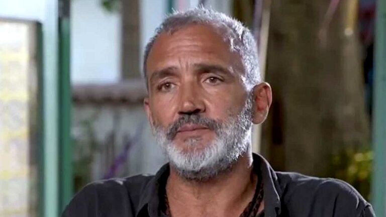 Diretor de cabelos grisalhos e barba branca durante entrevista em programa de televisão