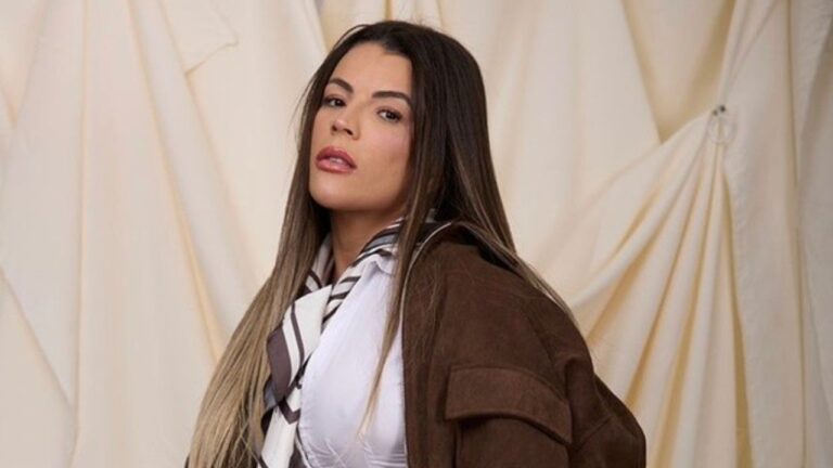 Rosana Ferreira posa com cabelo longo liso e look marrom e branco diante de fundo com tecido claro em ensaio fotográfico