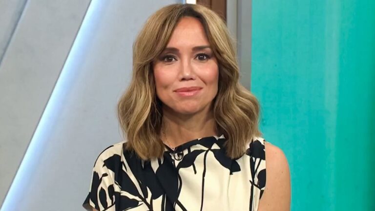 Apresentadora com vestido estampado olha para câmera durante telejornal em estúdio com fundo azul