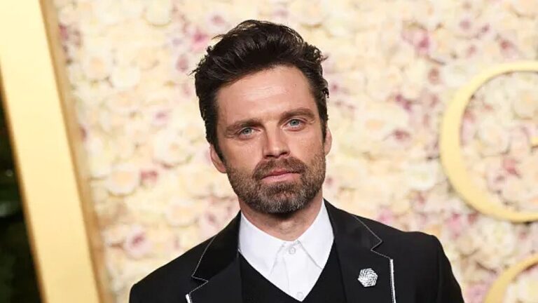 Sebastian Stan posa de terno preto durante premiação com painel floral ao fundo