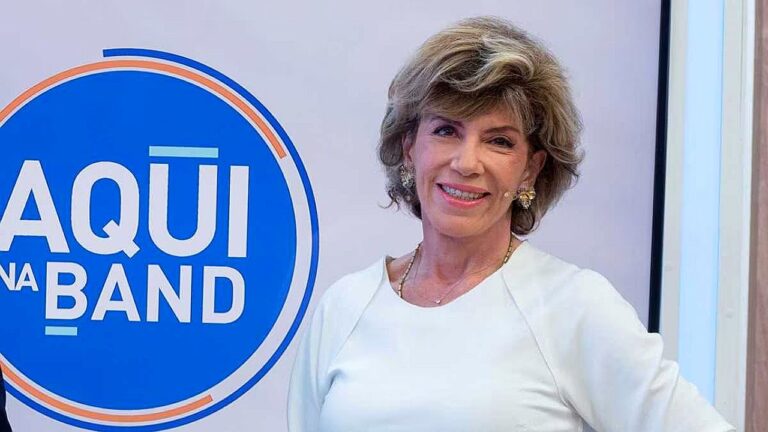 Mulher sorri ao lado do logotipo do programa Aqui na Band em estúdio da emissora