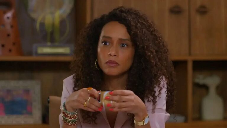 Mulher de cabelo cacheado segura xícara com expressão séria em cena de novela ou série brasileira