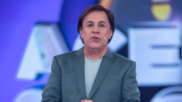 Tom Cavalcante apresentando o Acerte ou Caia! com microfone no rosto e cenário iluminado ao fundo