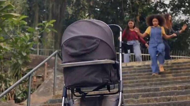 Carrinho de bebê parado em escadaria enquanto crianças correm ao fundo em cena de novela