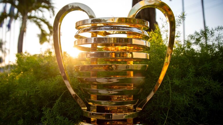 Troféu dourado da Copa do Nordeste posicionado ao ar livre com luz do pôr do sol entre árvores e folhagens ao fundo