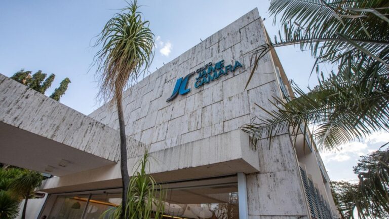 Fachada do Grupo Jaime Câmara com logotipo da empresa em prédio cercado por árvores e palmeiras
