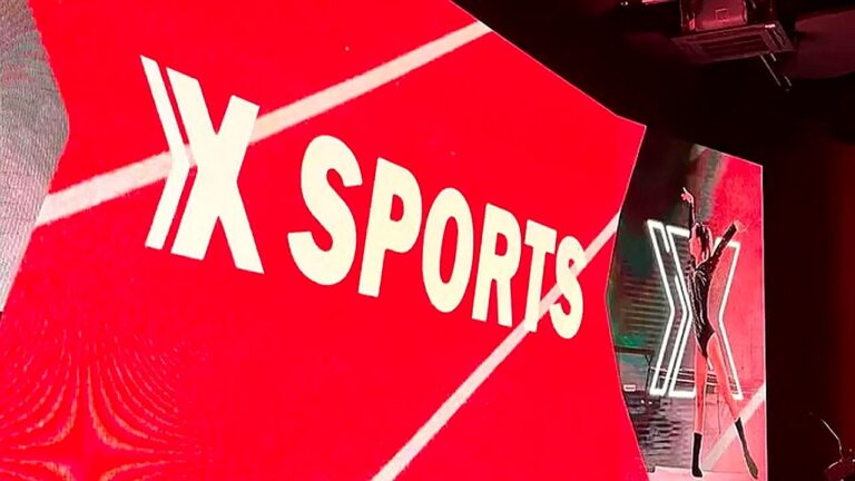 Logotipo do XSports exibido em painel vermelho durante transmissão esportiva em estúdio