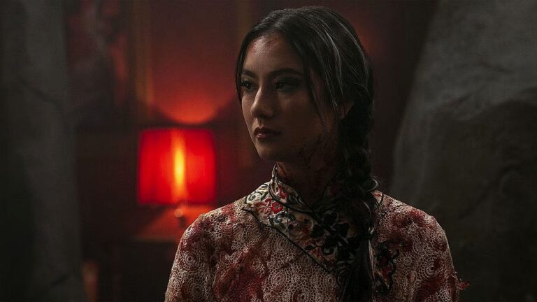 Adeline Rudolph com trança lateral e traje oriental em cena sombria em série