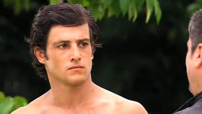 Alexandre Slaviero sem camisa em cena de Malhação com expressão séria durante confronto ao ar livre
