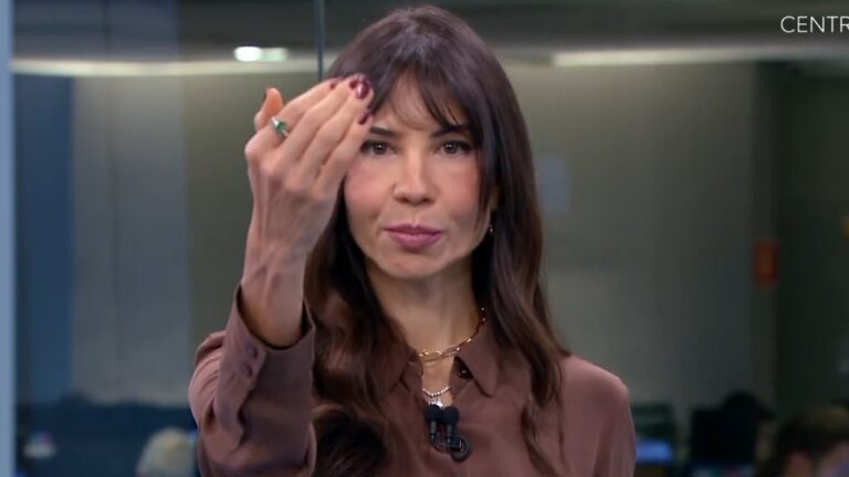 Amanda Klein de blusa marrom faz gesto com a mão durante apresentação do SBT News em estúdio de redação