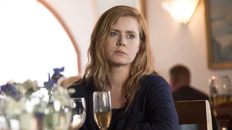 Amy Adams com expressão séria sentada à mesa de restaurante em cena de filme ou série