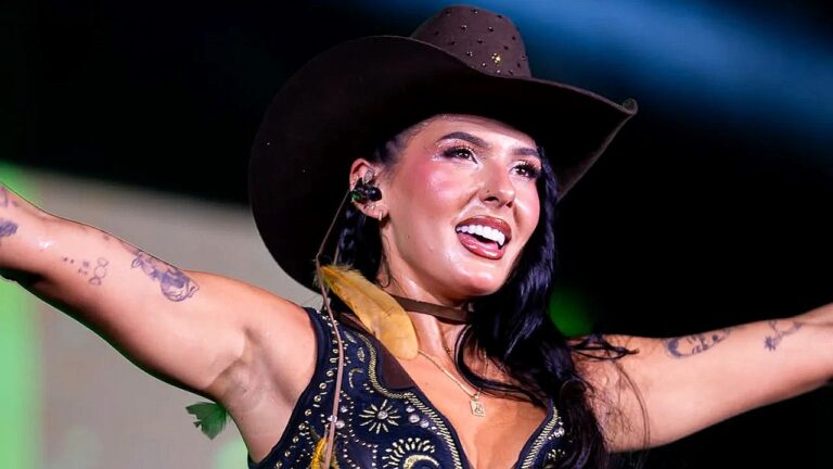 Ana Castela canta com chapéu de cowboy e braços abertos durante apresentação em show sertanejo ao vivo