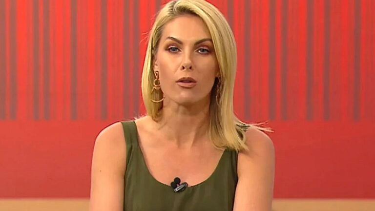 Ana Hickmann apresenta programa de televisão com vestido verde e cenário em tons de vermelho ao fundo