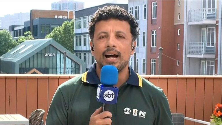 Repórter do SBT segura microfone durante entrada ao vivo em cobertura esportiva diante de prédios urbanos