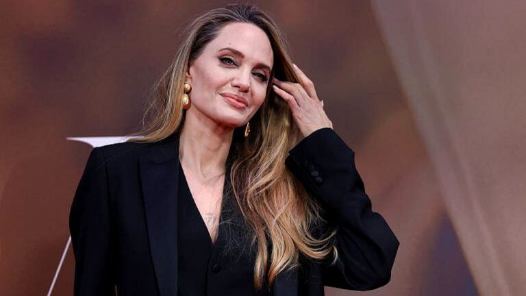 Angelina Jolie posa de blazer preto e brincos dourados durante evento de divulgação de filme em tapete vermelho