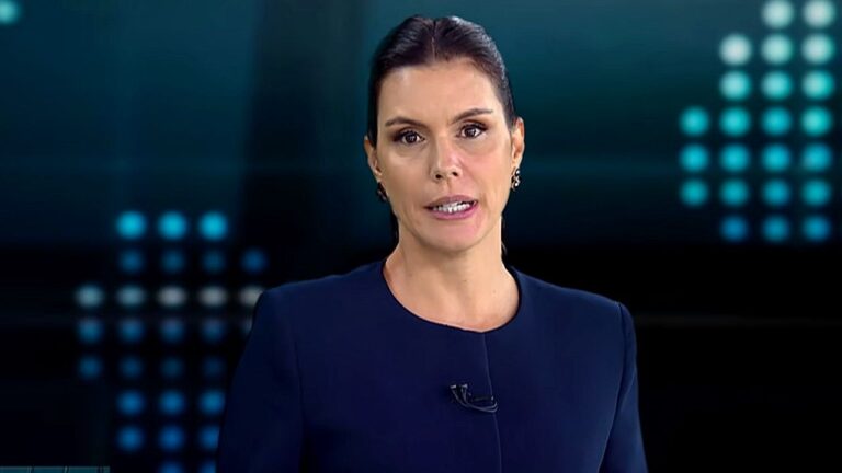 Camila Busnello apresenta telejornal com expressão séria em estúdio de notícias com painel digital ao fundo