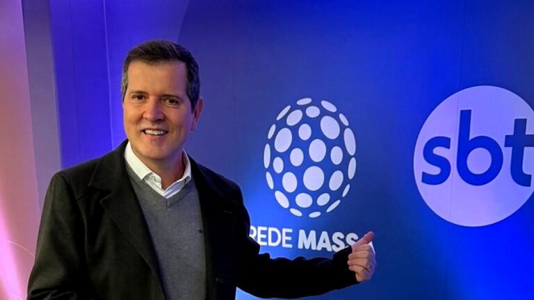 Executivo da Rede Massa aponta para logotipos da emissora e do SBT em parede iluminada da sede da empresa