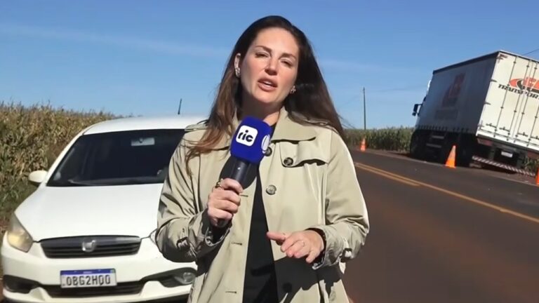 Carolina Barufatti com microfone da Ric TV reporta à beira de rodovia com carro e caminhão ao fundo no Balanço Geral