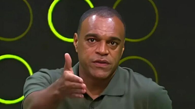 Homem de camisa polo gesticula com a mão estendida enquanto fala de forma enfática em programa de debates com cenário escuro e círculos luminosos verdes ao fundo