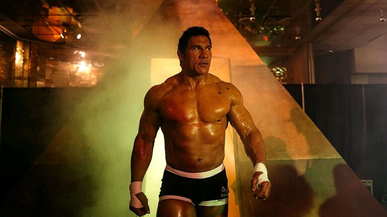 Dwayne Johnson com físico musculoso e tronco à mostra durante entrada em evento de luta com iluminação dramática ao fundo