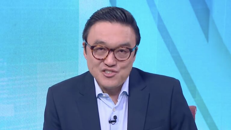 Fernando Nakagawa, de terno azul e óculos, fala no estúdio da CNN Brasil