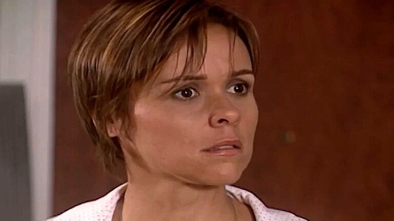 Giulia Gam com cabelo curto e expressão apreensiva em cena de novela dentro de casa