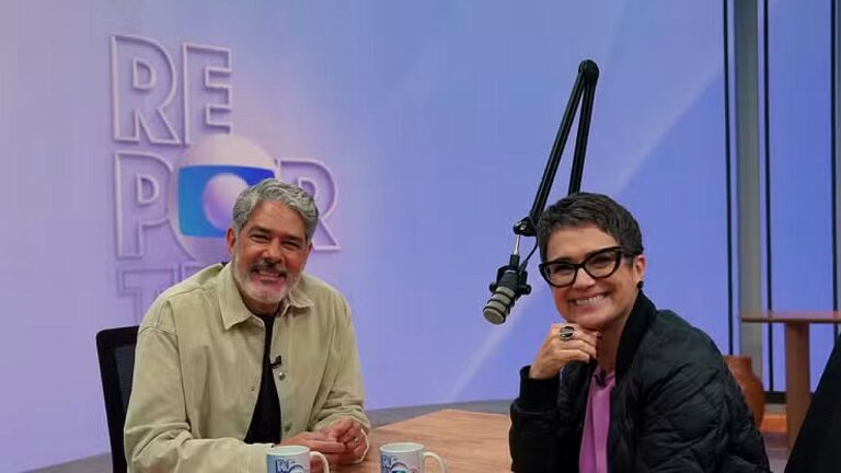 William Bonner e Sandra Annenberg posam sorrindo em estúdio de podcast com microfone suspenso e canecas sobre a mesa