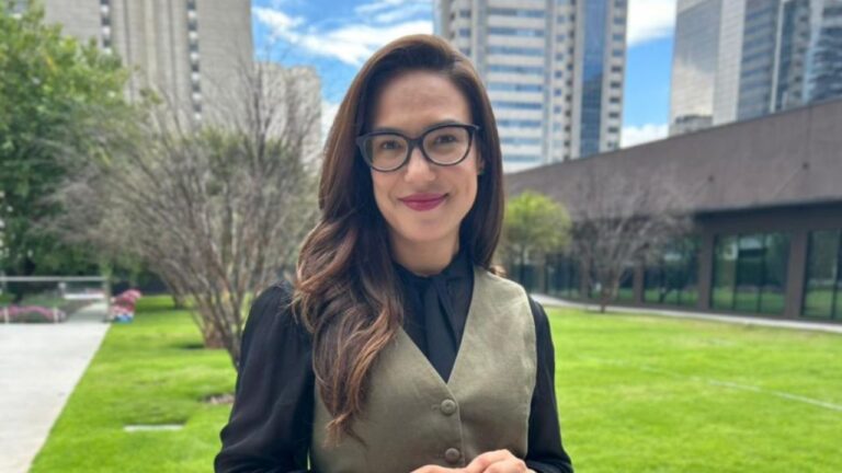 Grace Abdou sorri para a câmera em área verde cercada por prédios durante gravação externa da Record