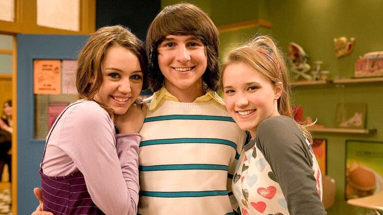 Mitchel Musso entre Miley Cyrus e Emily Osment sorrindo em cena da série Hannah Montana