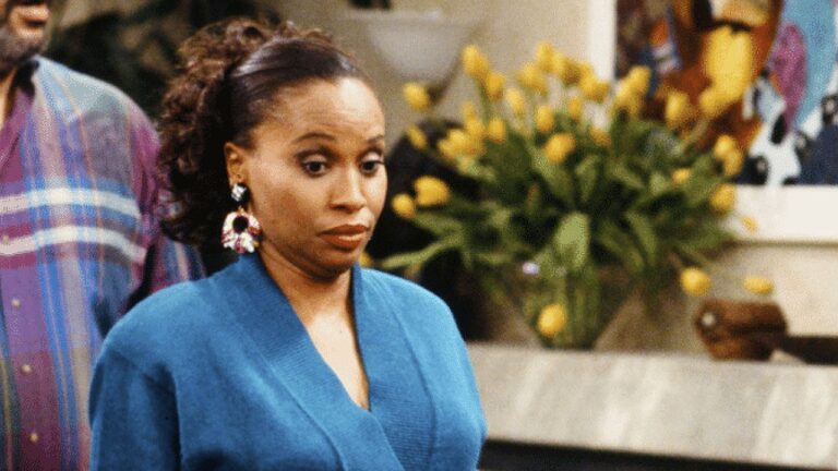 Jenifer Lewis com expressão de surpresa usando roupa azul em cena de série de comédia dentro de uma casa