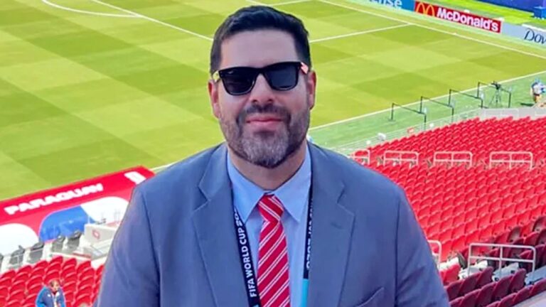 Jorge Chipi posa em estádio da Copa do Mundo com credencial da Fifa e terno durante cobertura esportiva
