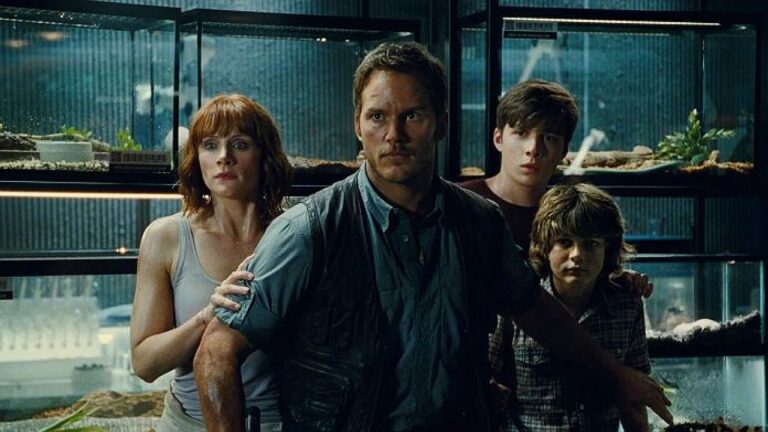 Chris Pratt, Bryce Dallas Howard e crianças encaram ameaça em cena do filme Jurassic World diante de terrários no parque jurássico