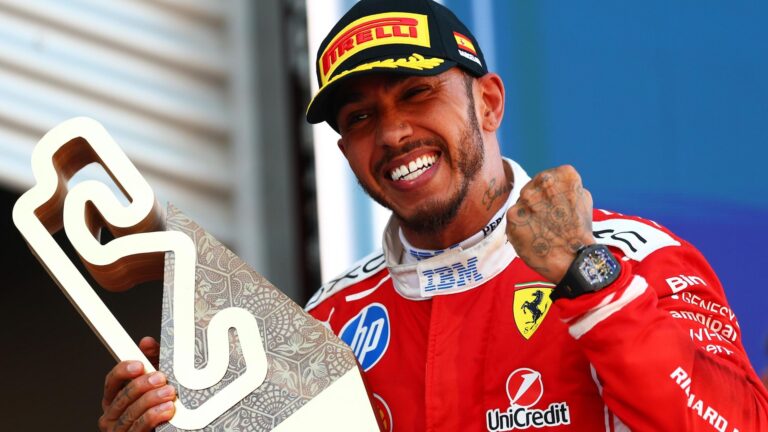 Lewis Hamilton, de macacão vermelho da Ferrari, sorri e ergue o punho enquanto segura troféu após vitória no GP de Barcelona-Catalunha da Fórmula 1