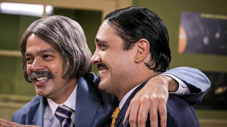 Lúcio Mauro Filho e Bruno Mazzeo caracterizados sorriem abraçados em cena de programa humorístico na televisão brasileira