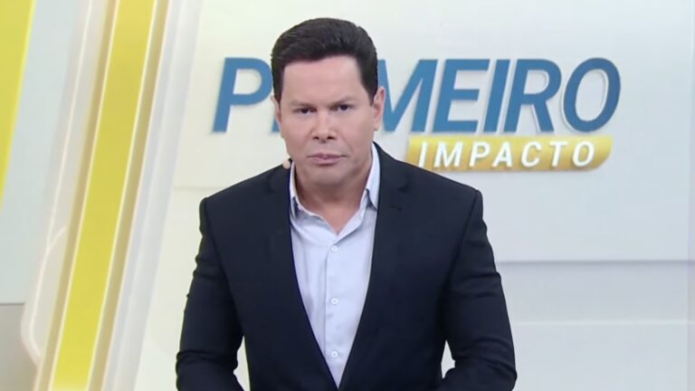 Marcão do Povo, de blazer escuro e camisa azul, encara a câmera no estúdio do Primeiro Impacto com logotipo do programa ao fundo