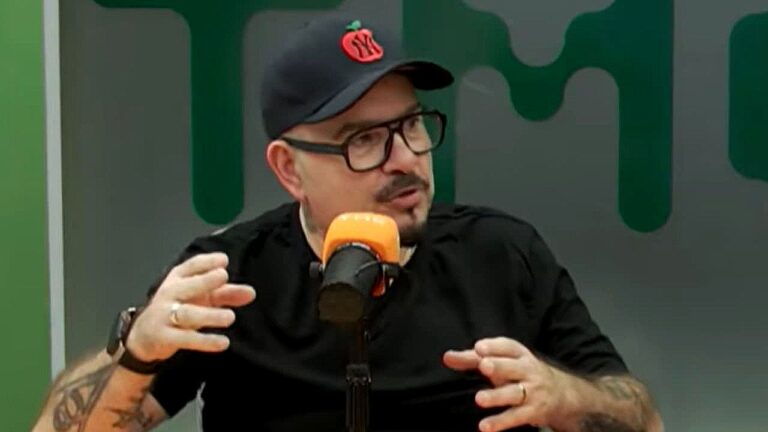 Apresentador de boné e óculos fala ao microfone durante gravação de programa em estúdio de rádio ou podcast