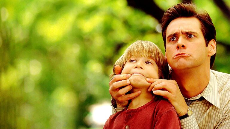 Jim Carrey faz careta enquanto segura o rosto de criança em cena da comédia O Mentiroso