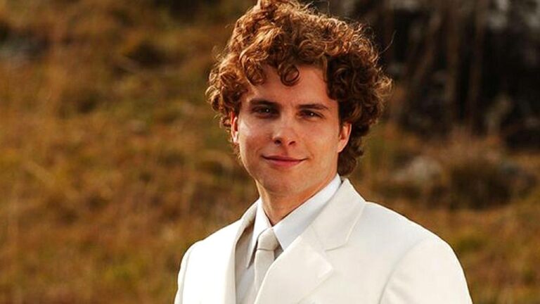 Personagem de cabelos cacheados usa terno branco em cena da novela O Profeta ao ar livre