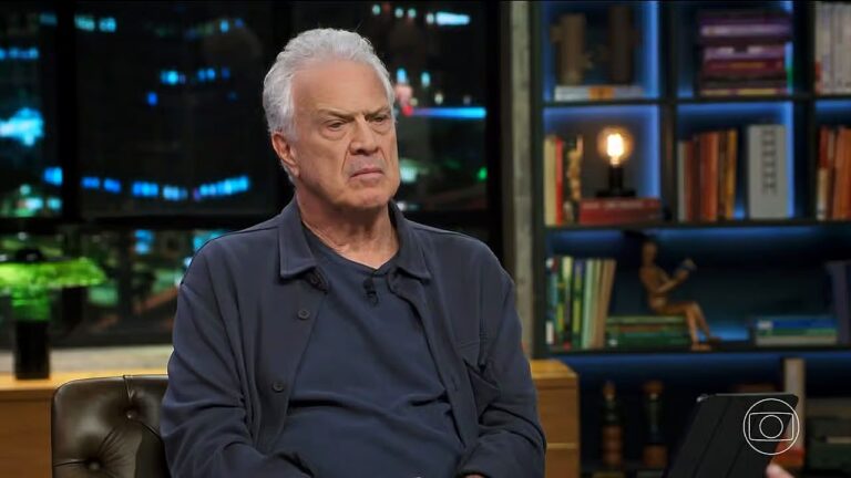 Pedro Bial com expressão séria durante entrevista em estúdio do Conversa com Bial com estante de livros ao fundo