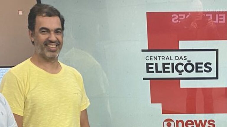 Pedro Godoy sorri diante de painel da Central das Eleições da GloboNews com logotipo do canal exibido ao fundo.