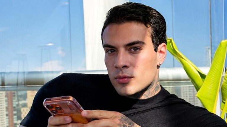 Rafa Marttinz segura celular e olha para a câmera em ambiente com vista urbana ao fundo