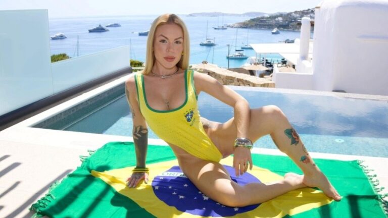 Ravena Hanniely de maiô amarelo posa sobre bandeira do Brasil à beira de piscina com mar e barcos ao fundo