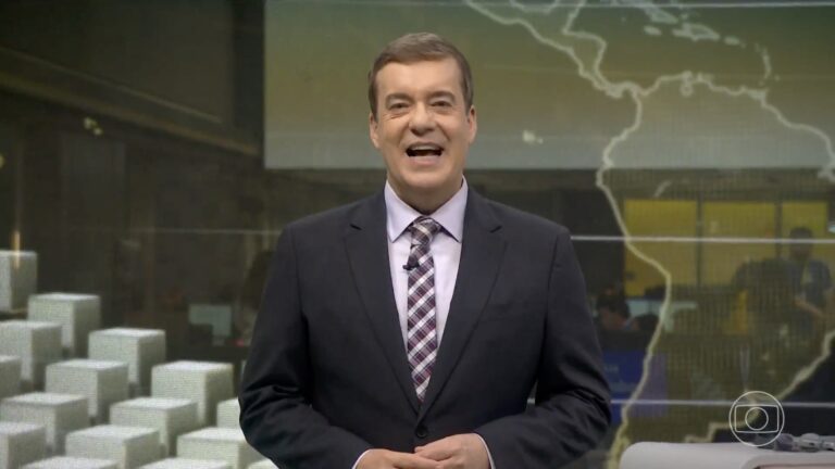 Roberto Kovalick, de terno escuro, sorri no estúdio do Jornal Hoje, com mapa ao fundo