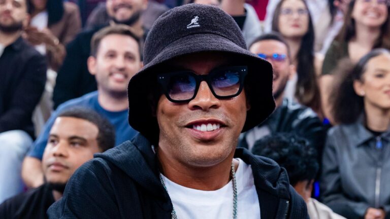 Ronaldinho Gaúcho usa chapéu preto e óculos escuros durante participação em programa de televisão com plateia ao fundo