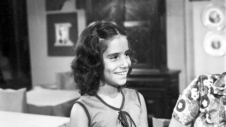Menina sorri em cena da novela Selva de Pedra ambientada na sala de uma casa em imagem em preto e branco