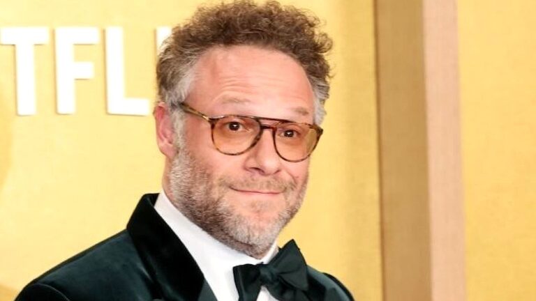 Seth Rogen posa de terno e gravata borboleta durante evento de estreia com logotipo da Netflix ao fundo