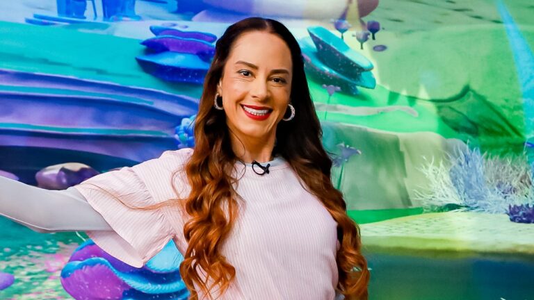 Silvia Abravanel sorri em estúdio do Sábado Animado diante de cenário colorido com elementos de animação ao fundo