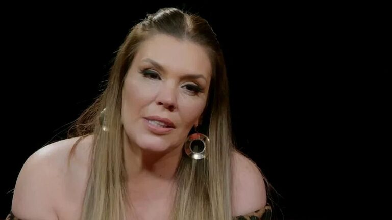 Simony emociona-se durante entrevista em estúdio usando brincos grandes e blusa preta ombro a ombro
