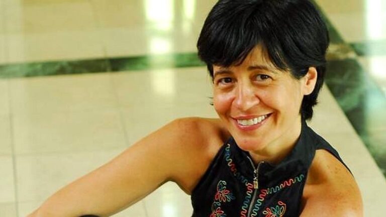 Thelma Guedes sorri para a câmera usando blusa preta sem mangas em retrato da autora de novelas