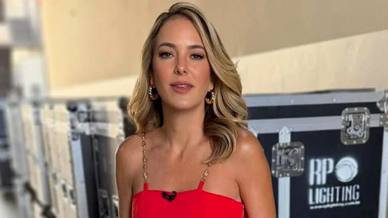 Ticiane Pinheiro com vestido vermelho e microfone de lapela nos bastidores de gravação em estúdio de televisão